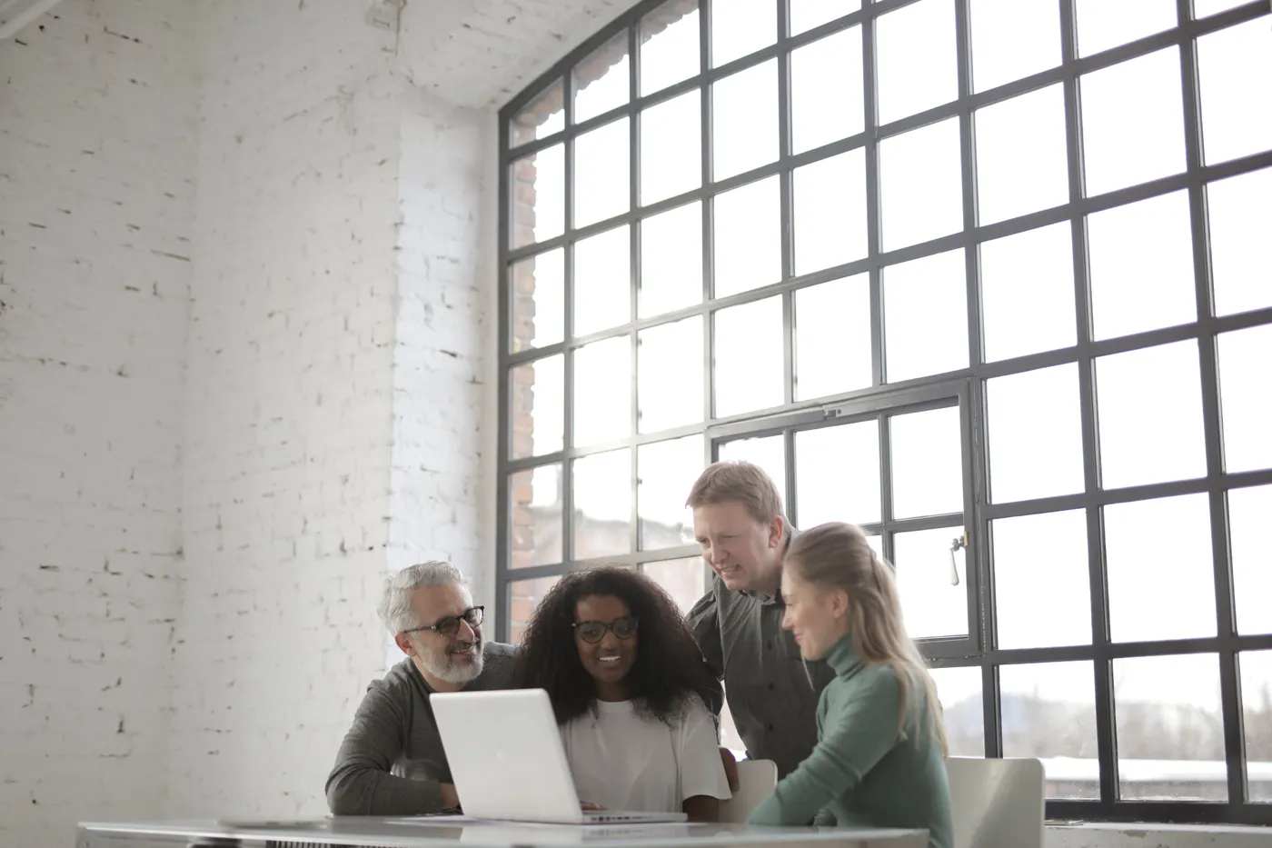 Four colleagues gathered around a laptop in a bright loft office