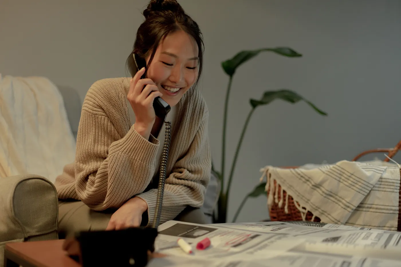 A woman laughing on a phone call at home, notes spread on the table