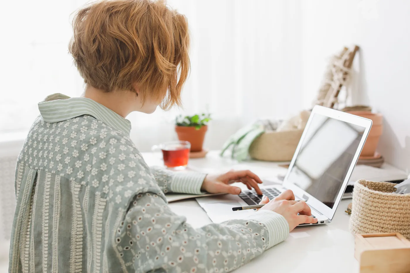 A woman working on her laptop at a bright desk at home