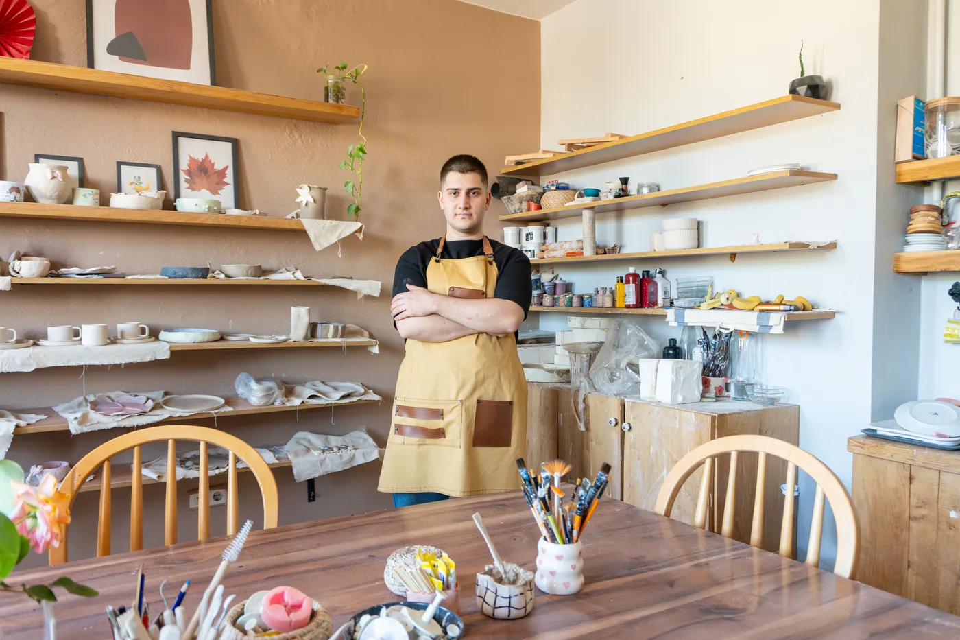 A potter in an apron standing in his bright pottery shop